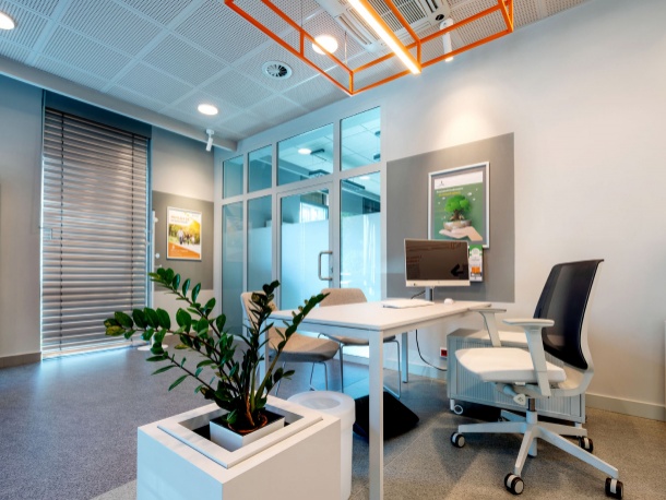 Wnętrze miejsca obsługi klienta PSG - fotel i krzesła przy biurku, komputer na biurku, donica z rośliną, plakaty na ścianie