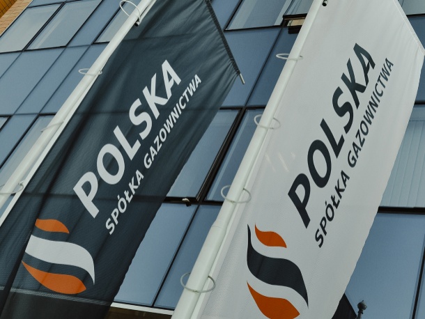 Dwie flagi z logotypem Polskiej Spółki Gazownictwa na tel szklanej ściany biurowca