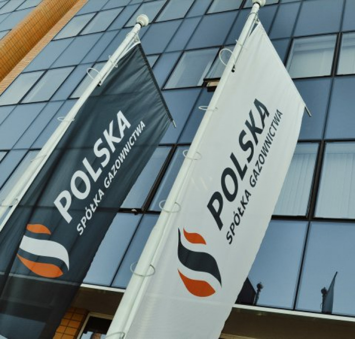 Flagi Polskiej Spółki Gazownictwa na tle biurowca ze szklanymi ścianami