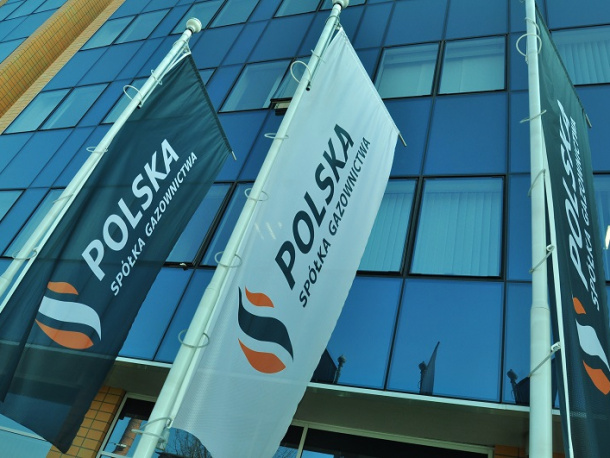 Flagi Polskiej Spółki Gazownictwa na tle biurowca ze szklanymi ścianami