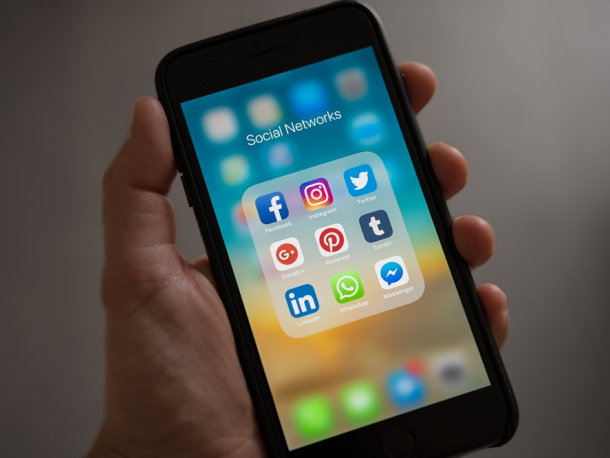 Trzymany w ręce smartfon, na ekranie ikonki aplikacji społecznościowych jak Facebook, Twitter czy Instagram