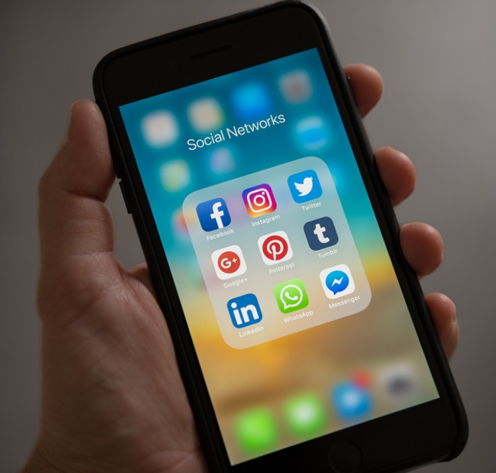 Trzymany w ręce smartfon, na ekranie ikonki aplikacji społecznościowych jak Facebook, Twitter czy Instagram
