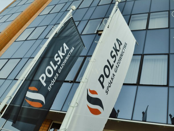 Flagi Polskiej Spółki Gazownictwa na tle biurowca ze szklanymi ścianami