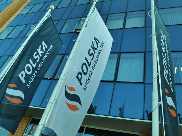 Flagi Polskiej Spółki Gazownictwa na tle biurowca ze szklanymi ścianami