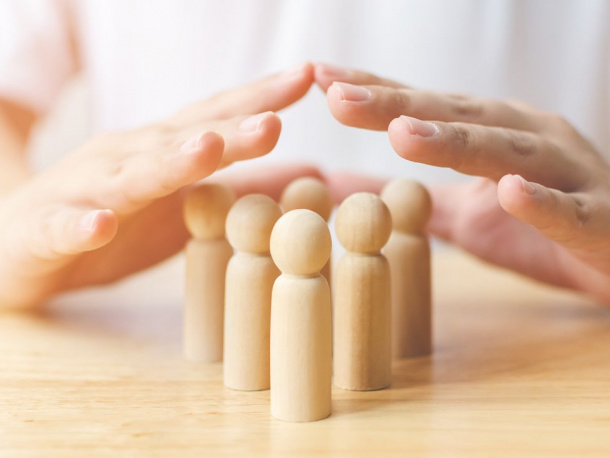 Dwie ręce oparte o stół, stykające się palcami, położone nad sześcioma drewnianymi figurkami przypominającymi ludzkie sylwetki