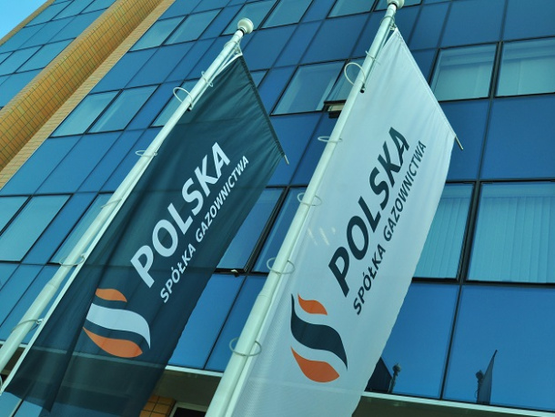 Flagi Polskiej Spółki Gazownictwa zawieszone na słupach na tle fasady szklanego biurowca