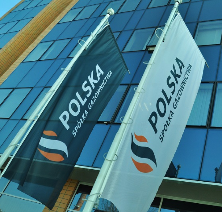 Flagi Polskiej Spółki Gazownictwa zawieszone na słupach na tle fasady szklanego biurowca