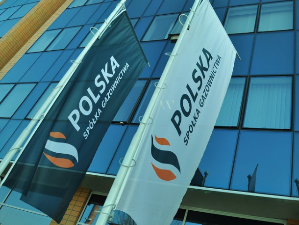 Flagi Polskiej Spółki Gazownictwa zawieszone na słupach na tle fasady szklanego biurowca