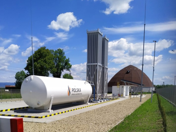 Stacja regazyfikacji Polskiej Spółki Gazownictwa wraz ze zbiornikiem, w tle drzewo i niebieskie niebo z chmurami