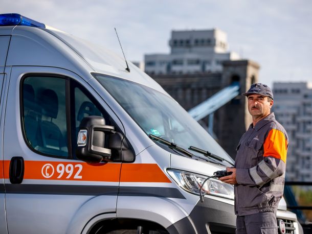 Pracownik pogotowia gazowego w ubraniu roboczym stoi obok samochodu pogotowia gazowego, w ręce trzyma detektor gazu