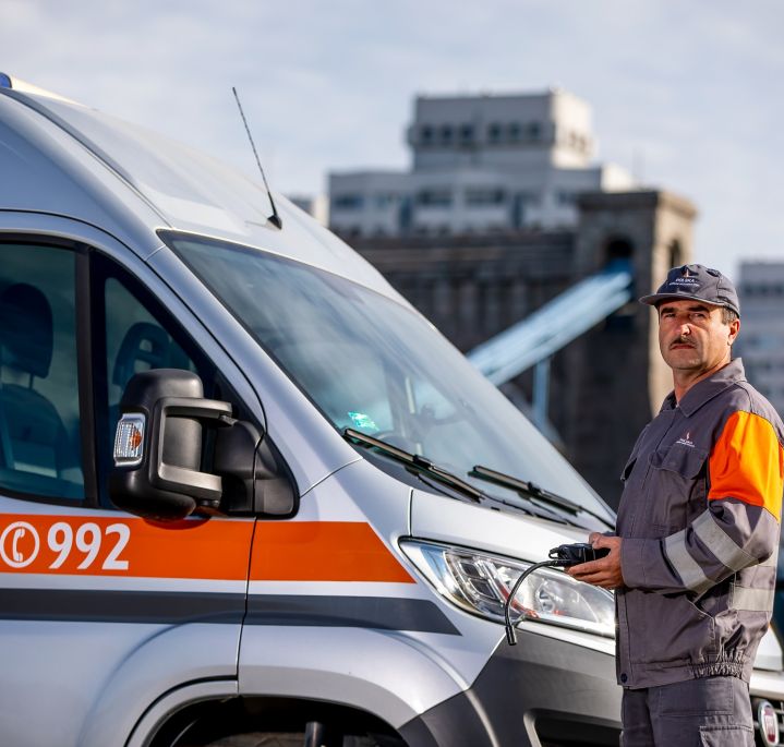 Pracownik pogotowia gazowego w ubraniu roboczym stoi obok samochodu pogotowia gazowego, w ręce trzyma detektor gazu