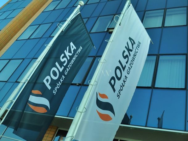 Flagi Polskiej Spółki Gazownictwa zawieszone na słupach na tle fasady szklanego biurowca