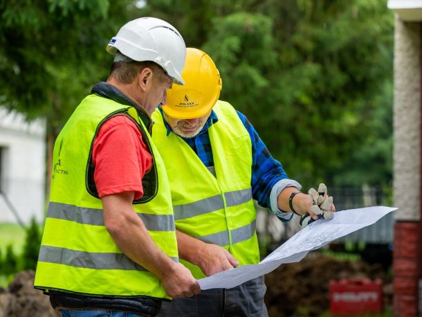 Dwóch pracowników PSG w kamizelkach odblaskowych ogląda rozłożony plan inwestycji