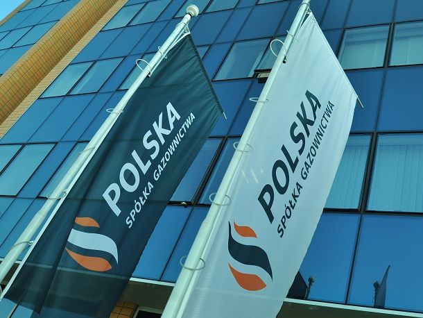 Flagi Polskiej Spółki Gazownictwa zawieszone na słupach na tle fasady szklanego biurowca