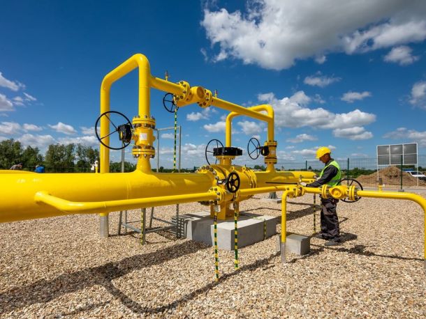 PSG gas infrastructure – yellow pipes with black valves, a PSG employee in work clothes standing next to them, blue sky and trees in the background