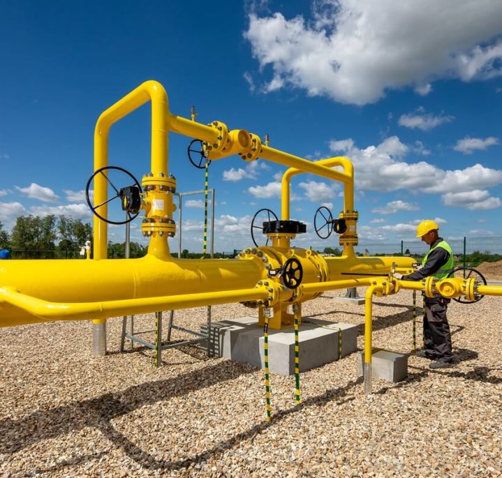 PSG gas infrastructure – yellow pipes with black valves, a PSG employee in work clothes standing next to them, blue sky and trees in the background