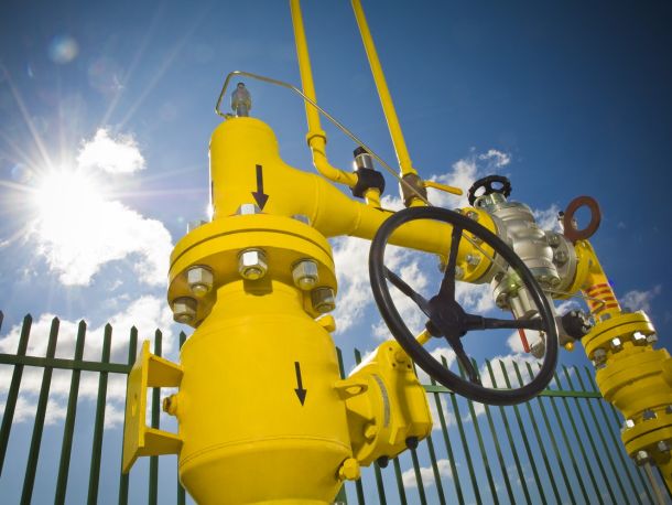 Żółte elementy infrastruktury gazowej (rury, manometr) na tle niebieskiego nieba i słońca