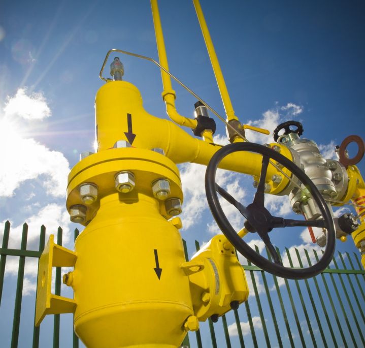 Yellow gas infrastructure elements (pipes, pressure gauge) against a blue sky and sun