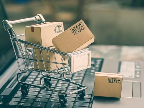 A photograph showing a small shopping trolley filled with cardboard boxes standing on the keyboard of an open laptop.