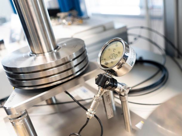 A silver pressure gauge connected to a gas pipe, next to metal laboratory equipment