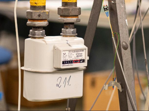 A grey gas meter connected to pipes, next to metal frame components and cables
