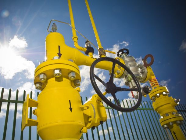 Yellow gas infrastructure components (pipes, pressure gauge) against a backdrop of blue sky and sunshine