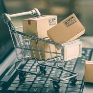 Model wózka zakupowego z pudełkami w środku stoi na klawiaturze otwartego laptopa
