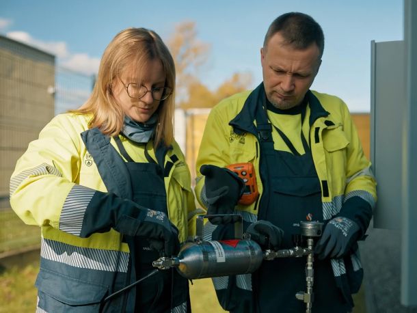 Zdjęcie przedstawiające dwoje pracowników PSG w w strojach roboczych (kurtki ochronne, rękawice) trzymających element infrastruktury gazowej
